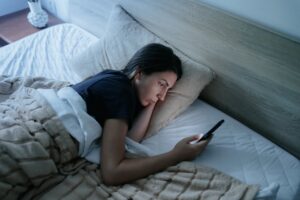Woman Lying in Bed at Night Using Smartphone, Struggling with Insomnia